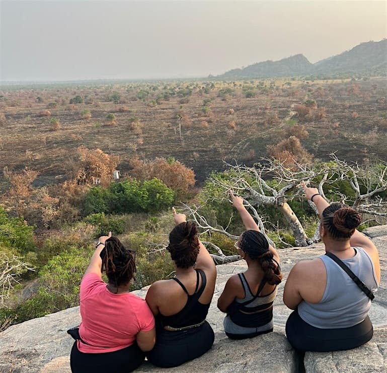 Four travellers seated on high ground, pointing out across the landscape below